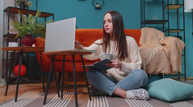 Young woman doing, planning home budget and counting money, girl checking dollar cash to pay utility bills. Young lady reviewing invoices on laptop computer, doing family business plan and tax return