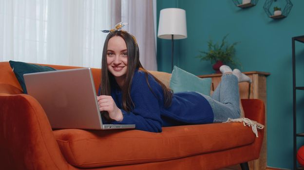 Young woman using laptop computer sitting on sofa working from home office. Adult girl elearning, browsing internet, doing online shopping, remote job, ordering food delivery on pc tech in living room
