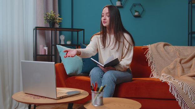 Young woman teacher consult student by laptop using modern tech for elearning at home room. Friendly adult girl freelancer tutor provide coaching by video call according to lesson plan on paper sheet