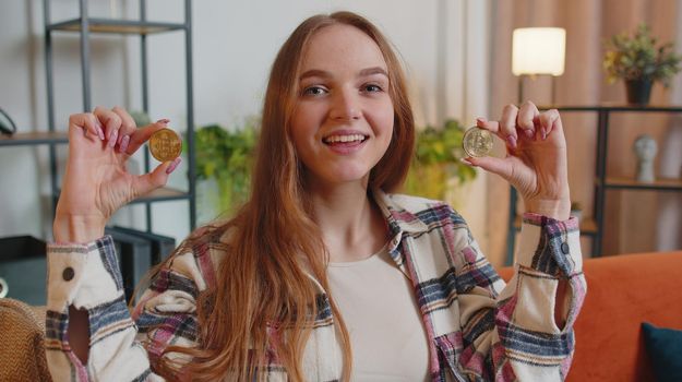 Woman freelancer holding two gold coins at home, successful developer programmer. Girl stock trader earning bitcoins after online monitoring trading operations. Increasing wealth, financial prosperity