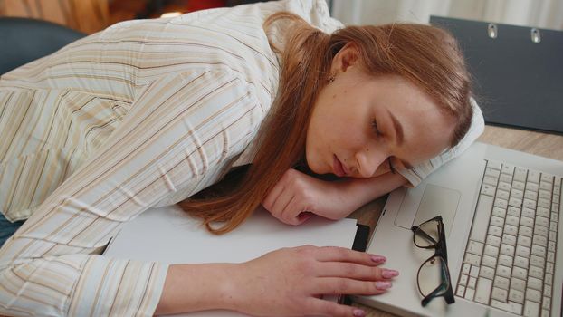 Exhausted bored lazy overworked businesswoman at home office falling asleep on table with laptop computer and crumpled sheets of paper. Girl feeling lack of energy after sleepless restless workday