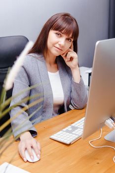 A brunette woman at a computer in the workplace. Business concept.