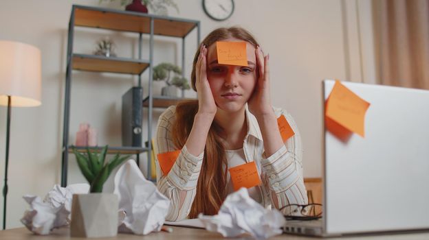 Bored overworked woman freelancer with pasted sticker notes sitting at desk having concentration problem creative crisis. Nervous adult girl confused by big routine work loading indoors at home office
