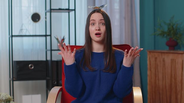Sad unhappy stylish teen girl in blue sweater wish, waiting for good luck, loses becoming surprised sudden lottery results, bad fortune, loss. Young adult woman indoor at home in living room on chair