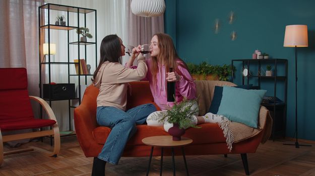 Drunk girls friends siblings clinking glasses of red wine cheering and drinking, celebrate birthday party hangout at home in living room. Two female women couple family celebrating new house purchase