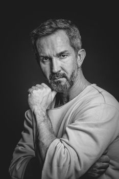 Sexy middle aged grey haired man leaned his face on hand looking at camera. Handsome middle aged man in black and white photo. Black and white portrait of attractive, beautiful, serious man.