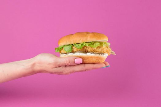 Female hand with tasty burger on a pink background