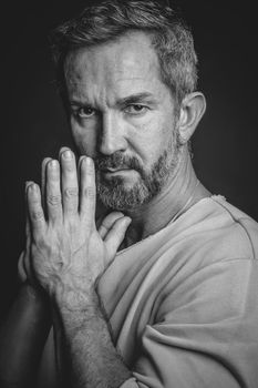 Grey haired mature man put hands together looking at camera. Handsome middle aged man in black and white photo. Black and white portrait of attractive, beautiful, serious man.