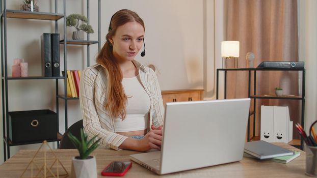Young woman with headset using laptop pc, talking, working customer support service operator at home office, in headphones with microphone in living room. Coronavirus quarantine distance isolation