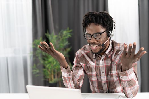 Gesturing african american freelancer looking at laptop with headphones having a group video call working distantly at home. Young student on distant leaning have a video group call.