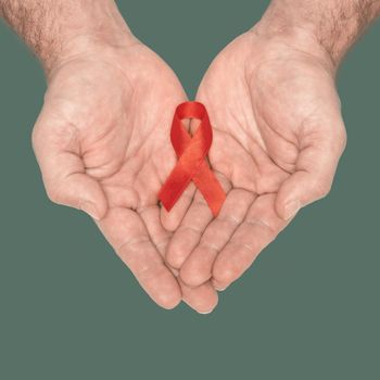 Red awareness ribbon bow on mans helping hands isolated on green background. HIV, AIDS world day. Social life issues concept. Aids charity fund concept. Healthcare and medicine concept.