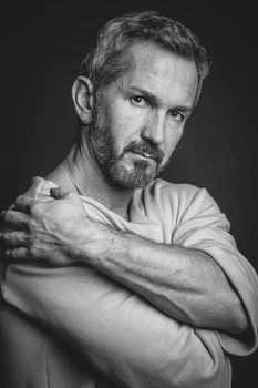 Black and white portrait of a serious grey haired mature man put hands around his shoulders looking at camera. Handsome middle aged man in black and white photo.