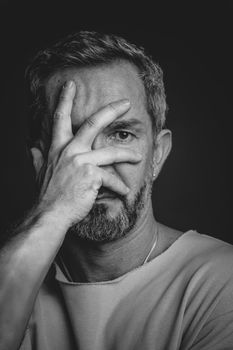 Mature grey haired man hide his face covered with hand looking sad or frightened. Handsome middle aged man in black and white photo. Black and white portrait of attractive, beautiful, serious man.