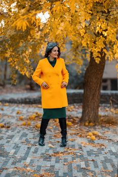 Beautiful woman walks outdoors in autumn. She is wearing a yellow coat and a green dress. Young woman enjoying the autumn weather. Autumn content
