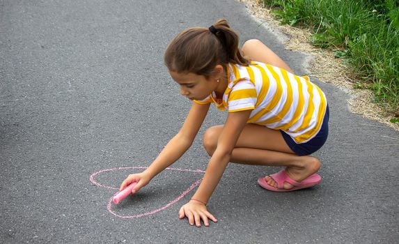 the child draws with chalk on the pavement, the heart is the sun. Nature. selective focus