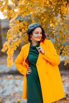 Beautiful woman walks outdoors in autumn. She is wearing a yellow coat and a green dress. Young woman enjoying the autumn weather. Autumn content