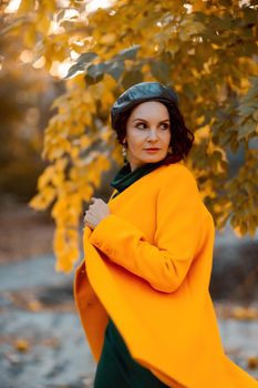 Beautiful woman walks outdoors in autumn. She is wearing a yellow coat and a green dress. Young woman enjoying the autumn weather. Autumn content