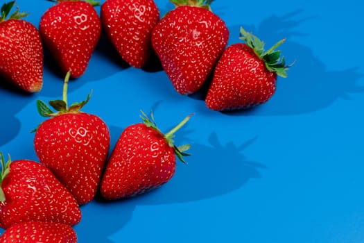 Bunch of strawberries on blue background. Red berry summer seasonal fruit