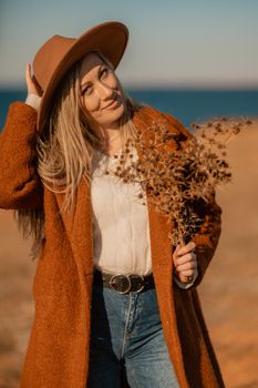 A woman walking along the coast near the sea. An elegant lady in a brown coat and a hat with fashionable makeup walks on the seashore.