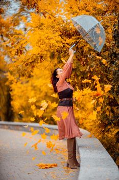 Beautiful girl in a dress with an umbrella in the autumn park. She holds him over her head, autumn leaves are falling out of him.