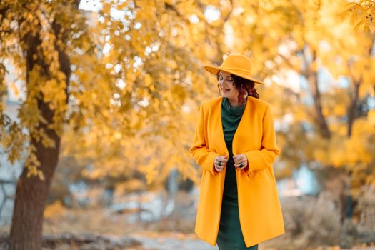 Beautiful woman walks outdoors in autumn. She is wearing a yellow coat, yellow hat and green dress. Young woman enjoying the autumn weather. Autumn content.