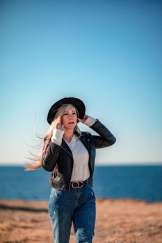 A blonde in a stylish black leather jacket walks along the seashore