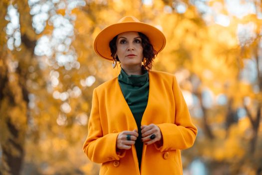 Beautiful woman walks outdoors in autumn. She is wearing a yellow coat, yellow hat and green dress. Young woman enjoying the autumn weather. Autumn content.