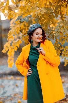 Beautiful woman walks outdoors in autumn. She is wearing a yellow coat and a green dress. Young woman enjoying the autumn weather. Autumn content