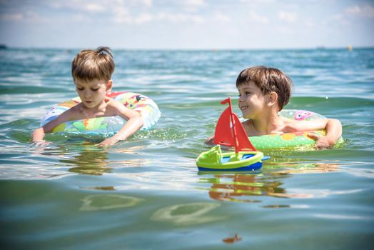 Happy kids have fun in sea surf on beach. Joyful couple of children on inflatable ring ride on breaking wave. Travel lifestyle, swimming activities in family summer camp. Vacations on tropical island.
