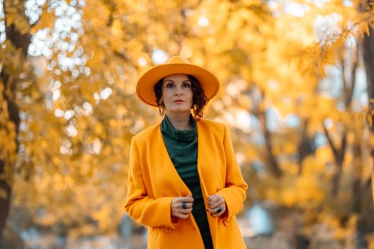 Beautiful woman walks outdoors in autumn. She is wearing a yellow coat, yellow hat and green dress. Young woman enjoying the autumn weather. Autumn content.