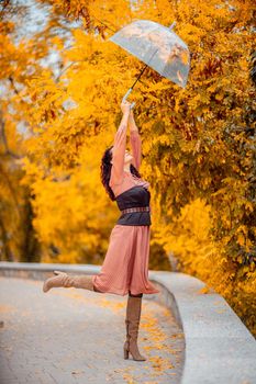 Beautiful girl in a dress with an umbrella in the autumn park. She holds him over her head, autumn leaves are falling out of him.