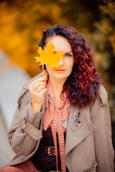 Beautiful girl walking outdoors in autumn. Smiling girl collects yellow leaves in autumn. Young woman enjoying autumn weather