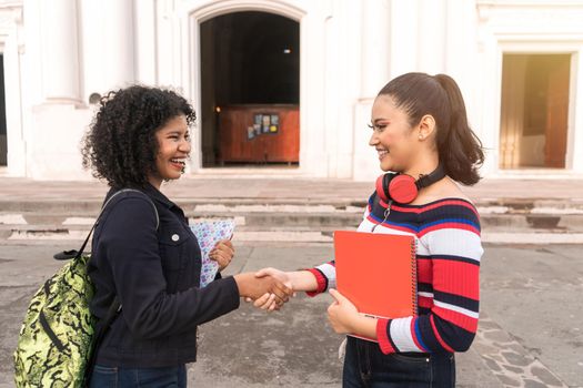 Two Latin students, one mestizo and one Hispanic shaking hands to work together and team up in their class activities. Both are outside a cathedral in Leon Nicaragua.