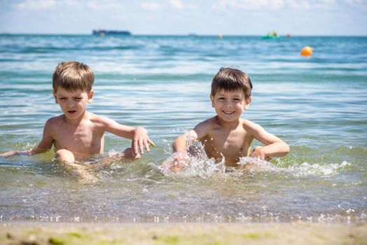 Happy family playing in blue water of swimming pool on a tropical resort at the sea. Summer vacations concept. Two brother kids are best friends.