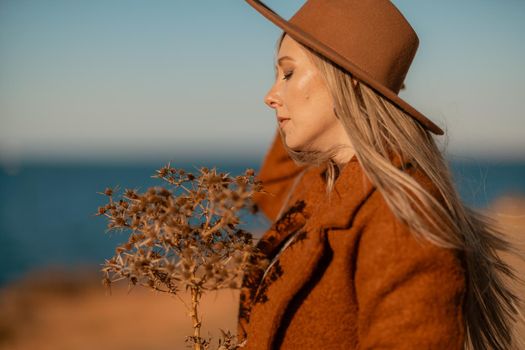 A woman walking along the coast near the sea. An elegant lady in a brown coat and a hat with fashionable makeup walks on the seashore.