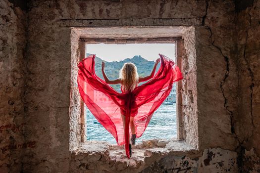 View of Balaklava Bay through an arched balcony in oriental style. The girl in a long red dress stands with her back. Abandoned mansion on the Black Sea coast.