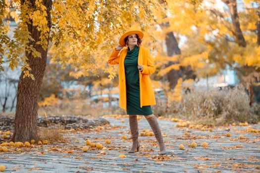 Beautiful woman walks outdoors in autumn. She is wearing a yellow coat, yellow hat and green dress. Young woman enjoying the autumn weather. Autumn content.