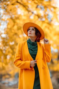 Beautiful woman walks outdoors in autumn. She is wearing a yellow coat, yellow hat and green dress. Young woman enjoying the autumn weather. Autumn content.