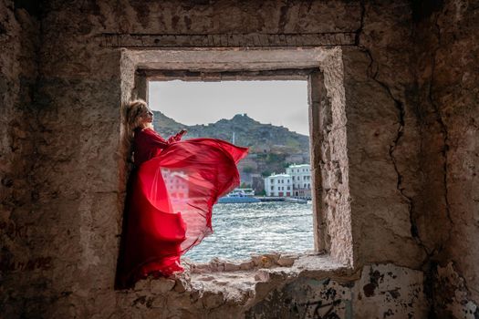 View of Balaklava Bay through an arched balcony in oriental style. The girl in a long red dress stands with her back. Abandoned mansion on the Black Sea coast.