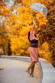 Beautiful girl in a dress with an umbrella in the autumn park. She holds him over her head, autumn leaves are falling out of him.