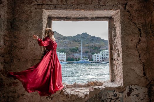 View of Balaklava Bay through an arched balcony in oriental style. The girl in a long red dress stands with her back. Abandoned mansion on the Black Sea coast.