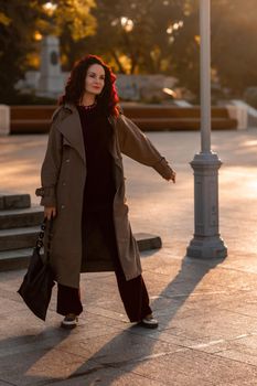 Outdoor fashion portrait of young elegant fashionable brunette woman, model in stylish hat, choker and light raincoat posing at sunset in European city