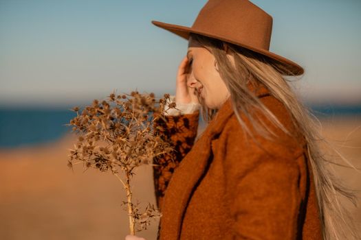 A woman walking along the coast near the sea. An elegant lady in a brown coat and a hat with fashionable makeup walks on the seashore.