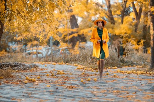 Beautiful woman walks outdoors in autumn. She is wearing a yellow coat, yellow hat and green dress. Young woman enjoying the autumn weather. Autumn content.