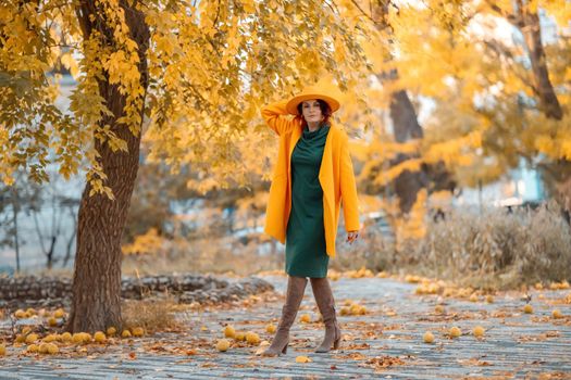 Beautiful woman walks outdoors in autumn. She is wearing a yellow coat, yellow hat and green dress. Young woman enjoying the autumn weather. Autumn content.