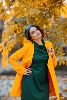 Beautiful woman walks outdoors in autumn. She is wearing a yellow coat and a green dress. Young woman enjoying the autumn weather. Autumn content