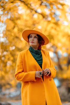 Beautiful woman walks outdoors in autumn. She is wearing a yellow coat, yellow hat and green dress. Young woman enjoying the autumn weather. Autumn content.