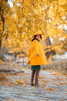 Beautiful woman walks outdoors in autumn. She is wearing a yellow coat, yellow hat and green dress. Young woman enjoying the autumn weather. Autumn content.