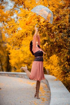 Beautiful girl in a dress with an umbrella in the autumn park. She holds him over her head, autumn leaves are falling out of him.