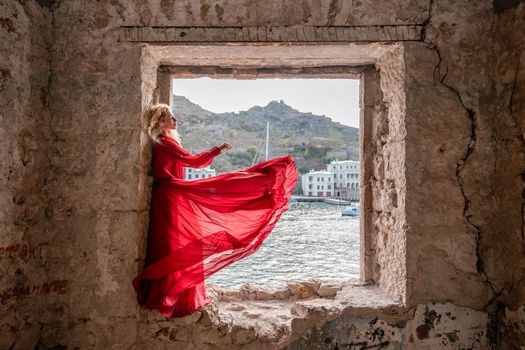 View of Balaklava Bay through an arched balcony in oriental style. The girl in a long red dress stands with her back. Abandoned mansion on the Black Sea coast.